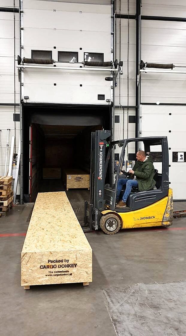 Handling van een lange industriële kist met heftruck in de laadruimte.